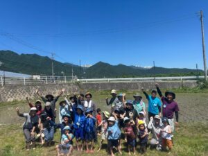 田んぼの教室の参加者の集合写真
田植えをした田んぼを背に立ち、腕を上げたポーズをして写っている